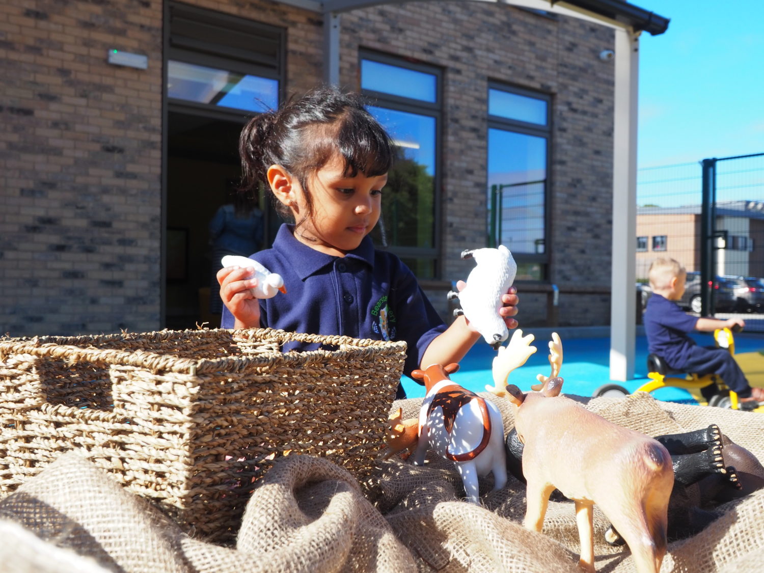 A child playing with animal toys outside on the academy grounds.