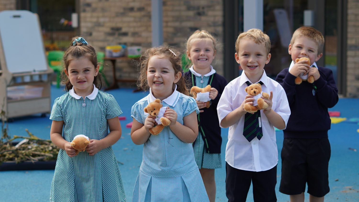 A group of children are pictured smiling for the camera outdoors whilst holding small teddy bears and smiling for the camera.